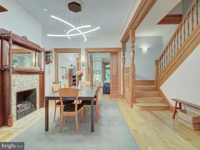 dining area with light hardwood / wood-style flooring, a notable chandelier, a fireplace, and ornamental molding