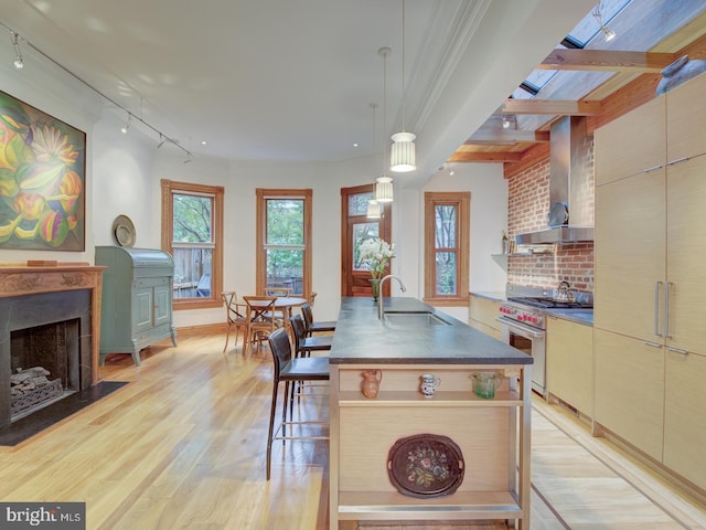 kitchen featuring light hardwood / wood-style floors, high end stove, wall chimney exhaust hood, pendant lighting, and sink