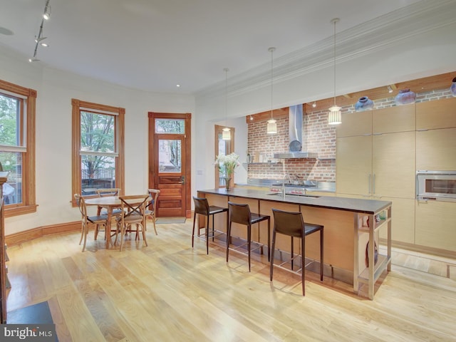 kitchen featuring hanging light fixtures, light hardwood / wood-style floors, rail lighting, a kitchen bar, and wall chimney range hood