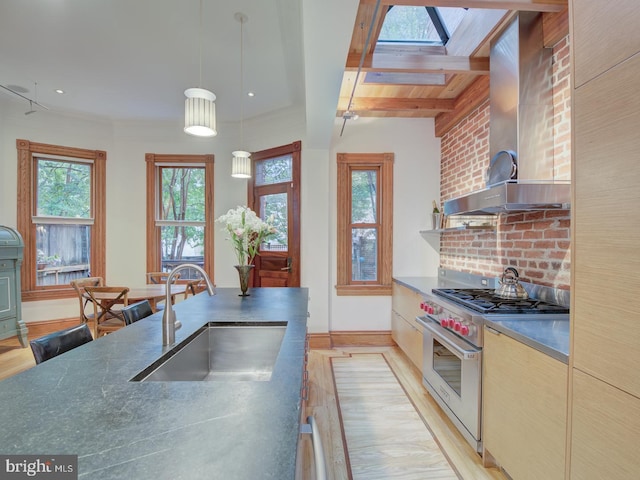 kitchen featuring premium range, wall chimney exhaust hood, light hardwood / wood-style flooring, decorative light fixtures, and sink