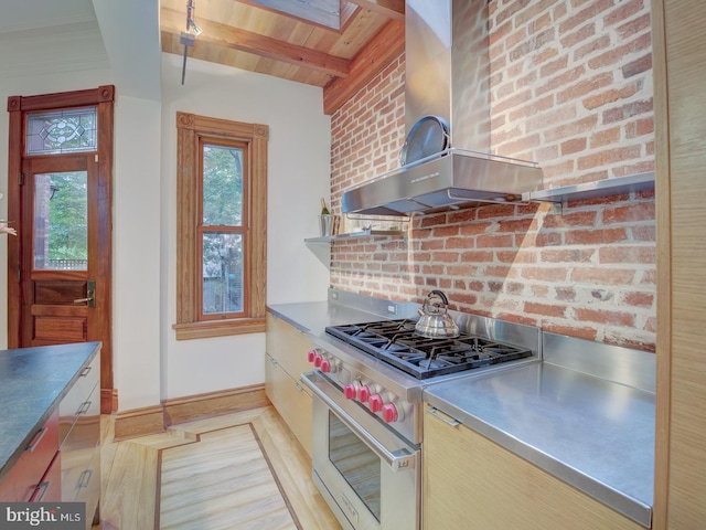 kitchen featuring wall chimney exhaust hood, premium stove, brick wall, and plenty of natural light