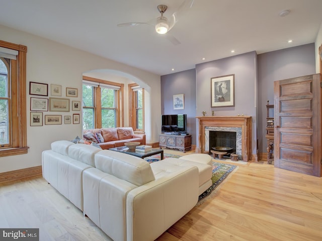 living room with a high end fireplace, light hardwood / wood-style floors, and ceiling fan