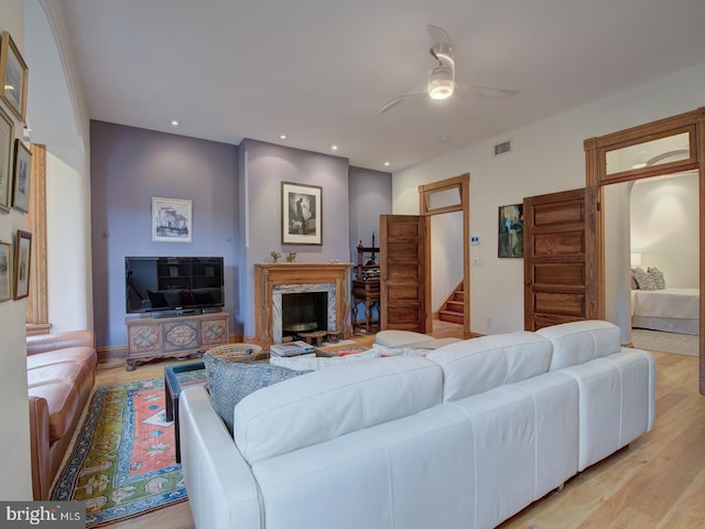 living room featuring light wood-type flooring, ceiling fan, and a premium fireplace