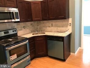 kitchen featuring dark brown cabinetry, sink, backsplash, stainless steel appliances, and light wood-type flooring