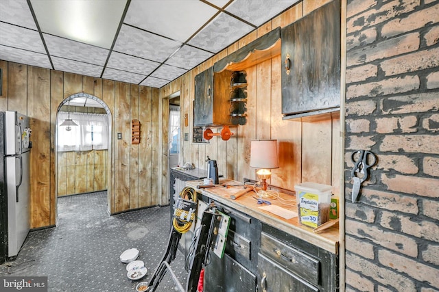 kitchen featuring brick wall, wooden walls, stainless steel fridge, and a paneled ceiling