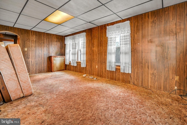 empty room with carpet floors, a drop ceiling, and wooden walls