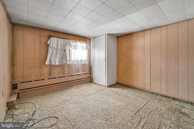 carpeted spare room with a baseboard heating unit and wood walls