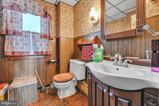 bathroom featuring a paneled ceiling, vanity, toilet, and wood walls