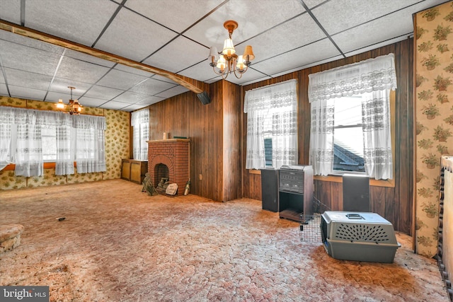 miscellaneous room featuring a brick fireplace, wooden walls, a paneled ceiling, a chandelier, and carpet floors