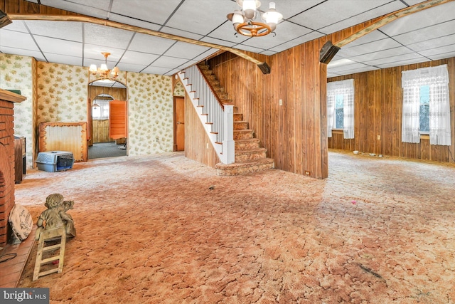 basement featuring an inviting chandelier, wooden walls, carpet floors, and a paneled ceiling