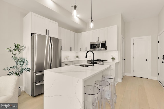 kitchen featuring appliances with stainless steel finishes, decorative light fixtures, a center island with sink, and white cabinets