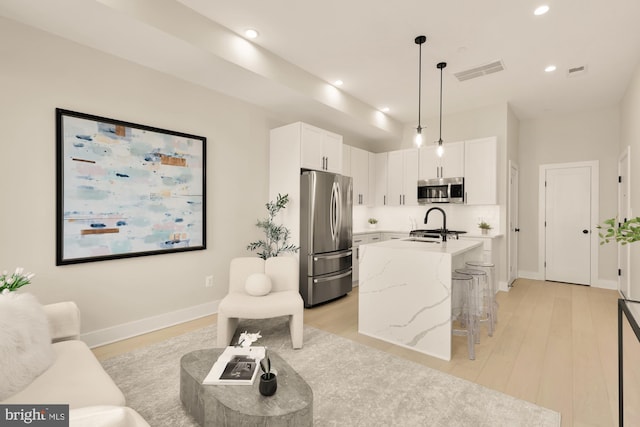 kitchen with white cabinets, hanging light fixtures, a center island with sink, appliances with stainless steel finishes, and light stone countertops