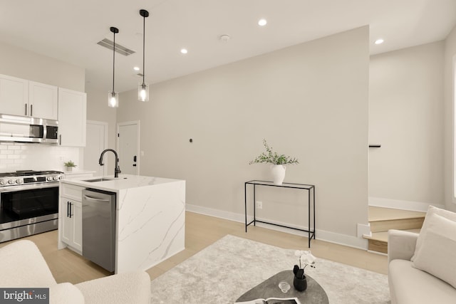 kitchen featuring light stone countertops, white cabinets, sink, appliances with stainless steel finishes, and decorative light fixtures