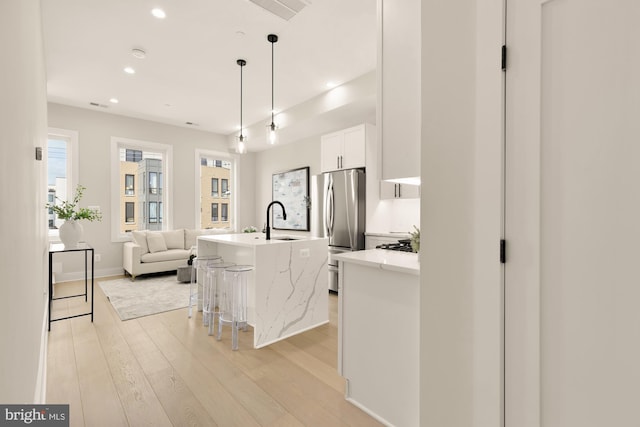 kitchen with white cabinets, pendant lighting, a kitchen island with sink, stainless steel refrigerator, and a kitchen breakfast bar