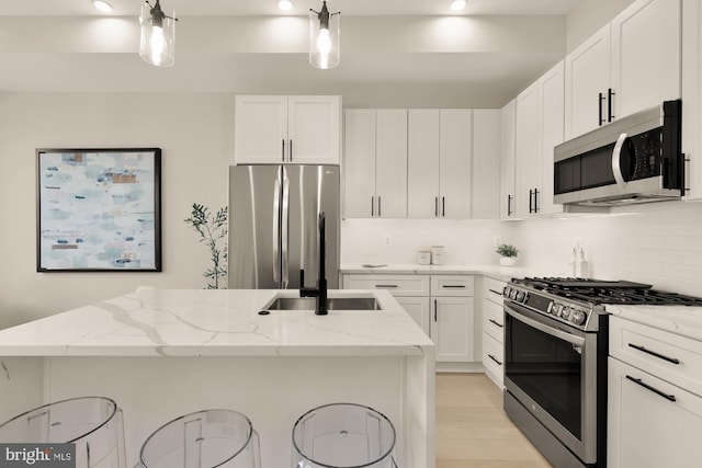 kitchen featuring pendant lighting, a breakfast bar area, light stone counters, white cabinets, and appliances with stainless steel finishes