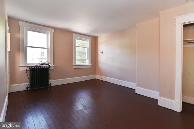 unfurnished bedroom featuring dark hardwood / wood-style floors, radiator heating unit, and a closet