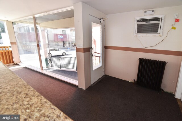 interior space featuring radiator heating unit, dark carpet, and a wall mounted air conditioner