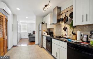 kitchen with wall chimney exhaust hood, an AC wall unit, black appliances, and white cabinetry