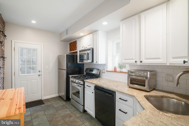 kitchen with light stone counters, tasteful backsplash, sink, white cabinetry, and appliances with stainless steel finishes