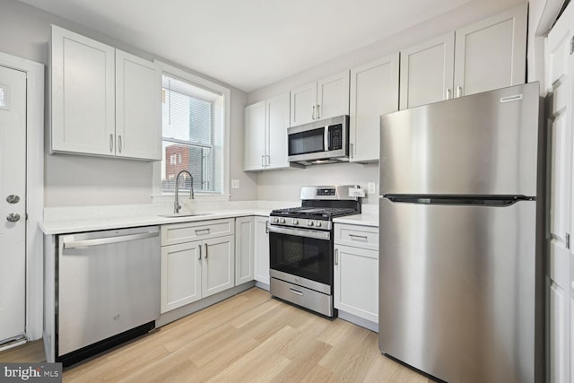 kitchen with light wood-type flooring, sink, stainless steel appliances, and white cabinets