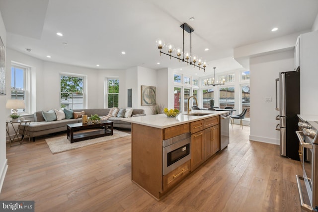 kitchen with pendant lighting, sink, light hardwood / wood-style flooring, stainless steel appliances, and a center island with sink