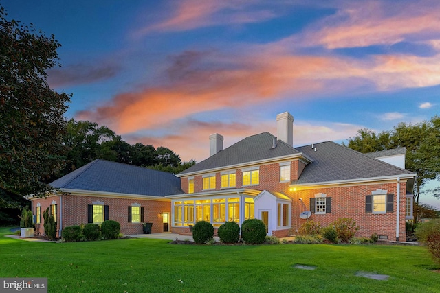 back house at dusk featuring a sunroom and a lawn