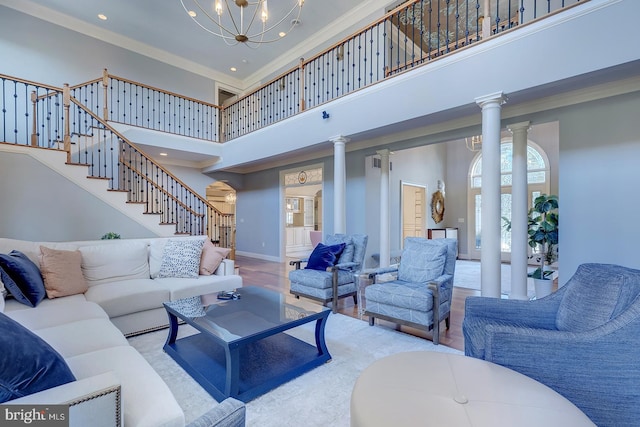 living room with crown molding, decorative columns, a high ceiling, and light wood-type flooring