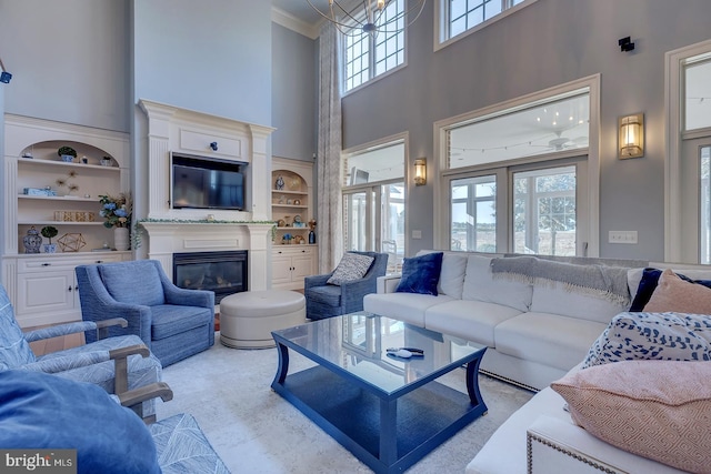 carpeted living room featuring crown molding, a notable chandelier, a high ceiling, and built in shelves