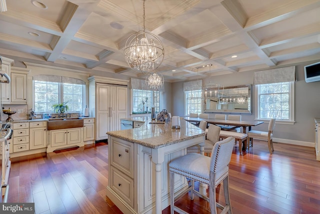 kitchen featuring cream cabinets, light stone countertops, wood-type flooring, a center island, and decorative light fixtures