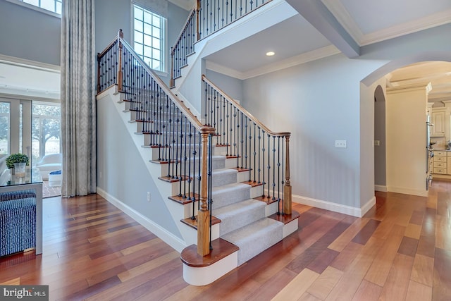 staircase featuring ornamental molding, hardwood / wood-style floors, beamed ceiling, and a high ceiling