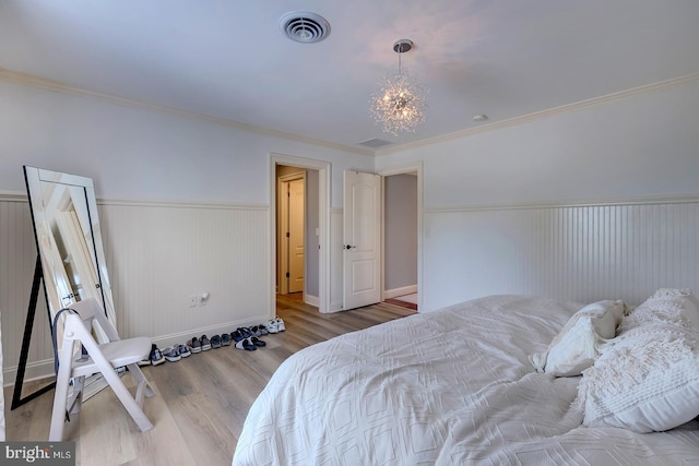 bedroom with an inviting chandelier, crown molding, light hardwood / wood-style floors, and wooden walls