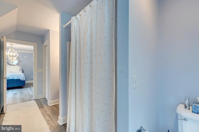 bathroom with lofted ceiling, toilet, wood-type flooring, an inviting chandelier, and walk in shower