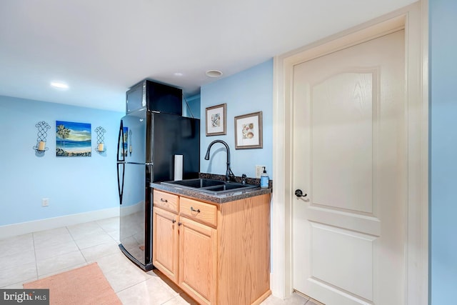 kitchen with black refrigerator, sink, light brown cabinetry, and light tile patterned floors