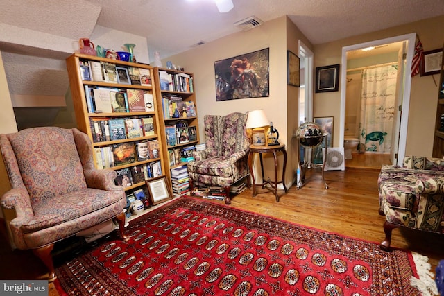 sitting room with wood-type flooring, vaulted ceiling, and a textured ceiling