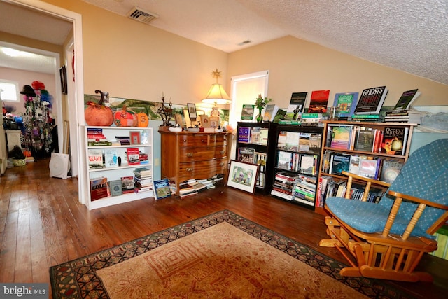 living area with a textured ceiling, lofted ceiling, and hardwood / wood-style floors