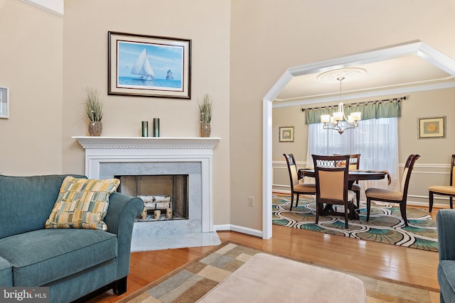 living room featuring hardwood / wood-style flooring, ornamental molding, a premium fireplace, and a chandelier