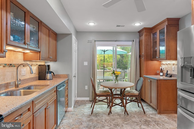 kitchen with sink, ceiling fan, appliances with stainless steel finishes, backsplash, and light stone counters