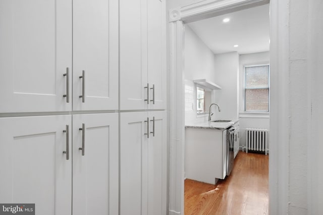 corridor with light hardwood / wood-style flooring, sink, and radiator heating unit