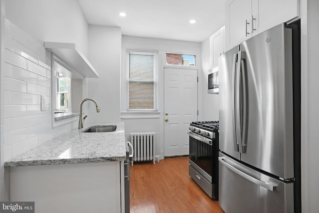 kitchen with white cabinetry, light stone countertops, stainless steel appliances, radiator, and sink