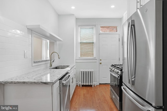 kitchen with sink, white cabinetry, light hardwood / wood-style flooring, stainless steel appliances, and radiator heating unit