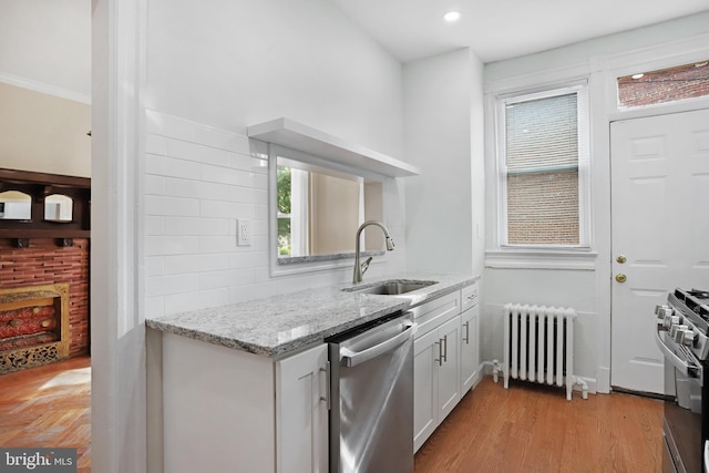 kitchen featuring white cabinets, sink, radiator heating unit, appliances with stainless steel finishes, and light stone countertops