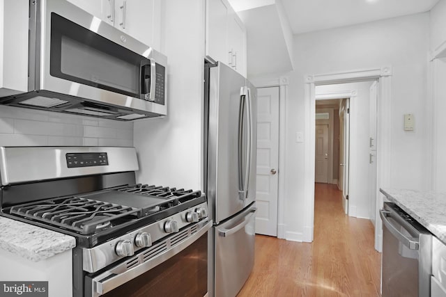 kitchen featuring backsplash, white cabinetry, stainless steel appliances, light stone countertops, and light hardwood / wood-style floors