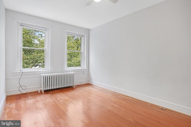 spare room with ceiling fan, radiator, and light wood-type flooring