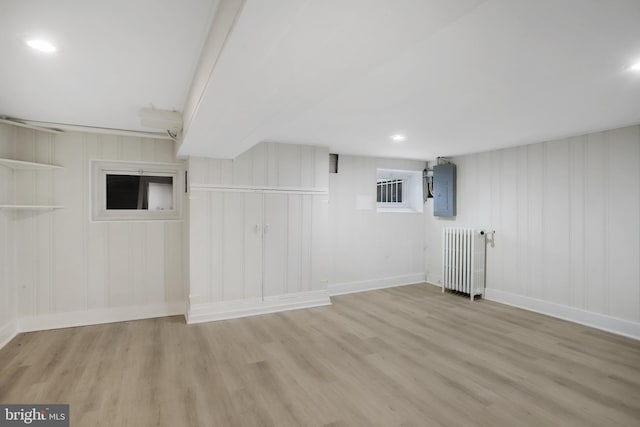 basement featuring radiator heating unit, wood walls, light hardwood / wood-style floors, and electric panel