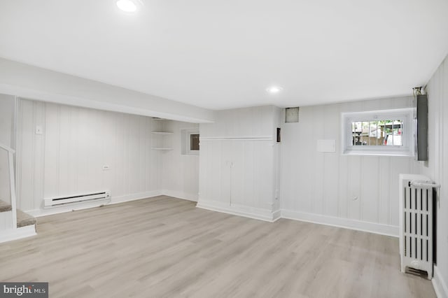 basement featuring wooden walls, radiator, light hardwood / wood-style flooring, and a baseboard radiator