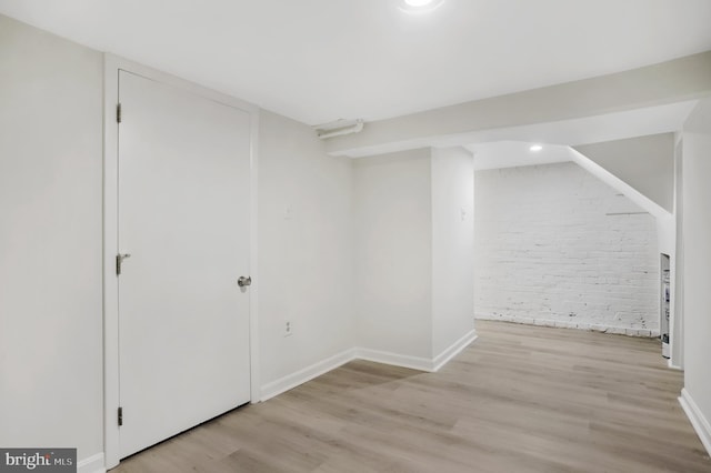 basement with light hardwood / wood-style floors and brick wall