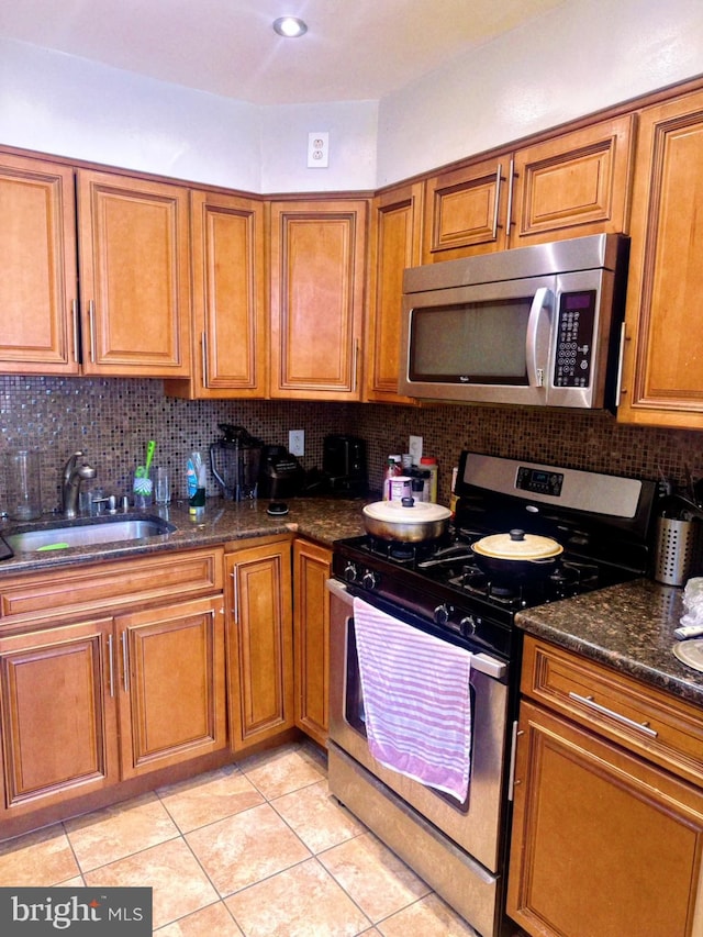 kitchen with appliances with stainless steel finishes, tasteful backsplash, light tile patterned floors, dark stone counters, and sink