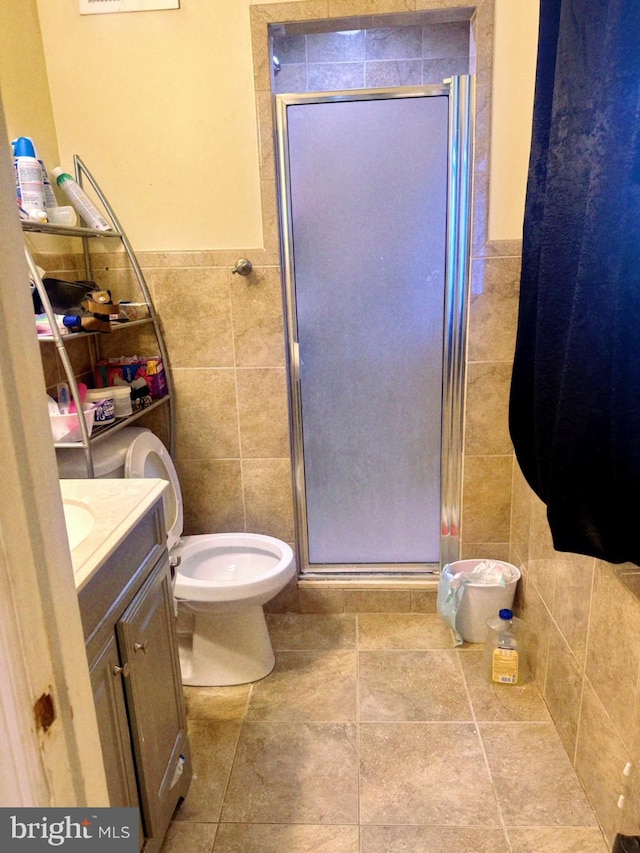 bathroom with tile walls, vanity, tile patterned flooring, a shower with door, and toilet