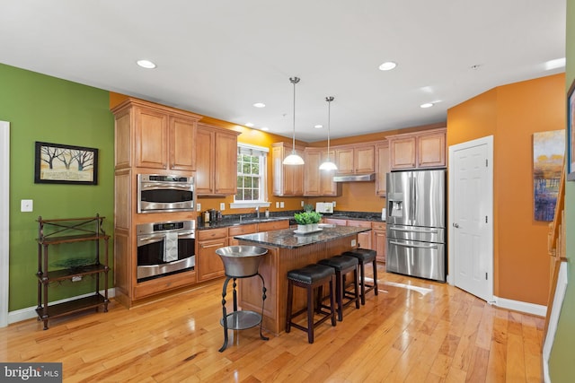 kitchen featuring light hardwood / wood-style floors, a kitchen island, dark stone countertops, stainless steel appliances, and hanging light fixtures