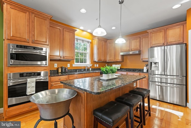 kitchen featuring sink, light hardwood / wood-style flooring, decorative light fixtures, appliances with stainless steel finishes, and a center island